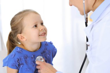 Doktor steteskopla küçük bir kızı muayene ediyor. Her zamanki tıbbi muayenede gülümseyen çocuk hasta. Tıp ve sağlık hizmetleri kavramları