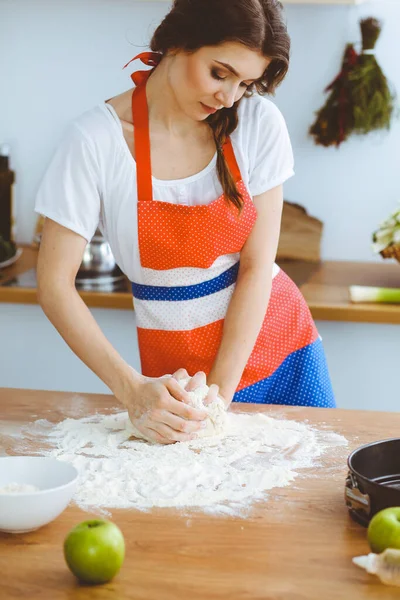 Jovem morena cozinhando pizza ou massa artesanal na cozinha. Dona de casa que prepara a massa de farinha na mesa de madeira. Conceito de alimentação, alimentação e saúde — Fotografia de Stock