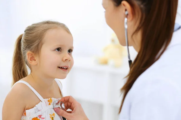 Arzt untersucht ein kleines Mädchen per Stethoskop. Glücklich lächelnder Kinderpatient bei der üblichen ärztlichen Untersuchung. Medizin- und Gesundheitskonzepte — Stockfoto