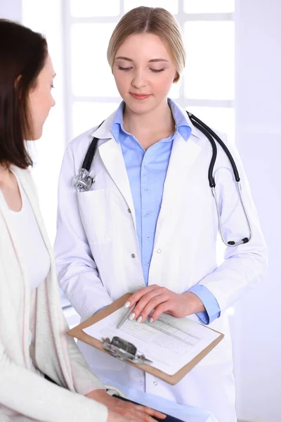 Mujer joven médico y paciente en el examen médico en el consultorio del hospital. Blusa de color azul del terapeuta se ve bien. Concepto de medicina y salud — Foto de Stock