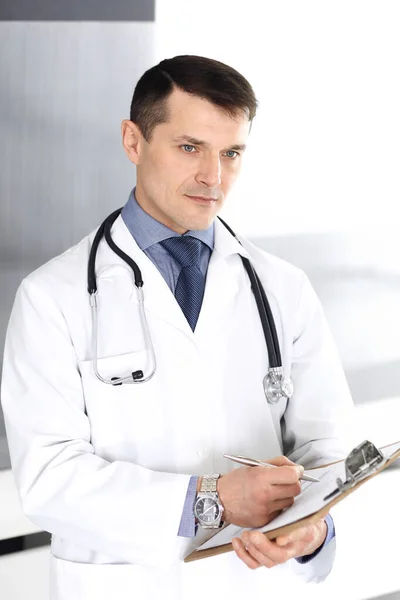 Dokter man met behulp van klembord voor het vullen van medicatie geschiedenis verslagen. Perfecte medische dienst in de kliniek. Artsen op het werk in het ziekenhuis. Begrippen geneeskunde en gezondheidszorg — Stockfoto