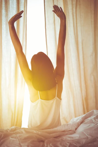 Woman stretching hands in bed after wake up, sun flare . Brunette entering a day happy and relaxed after good night sleep and back view. Concept of a new day and joyful weekend — Stock Photo, Image