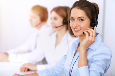 Merkezi ara. Güneşli ofiste kulaklık kullanan güzel bir iş kadınına odaklan.