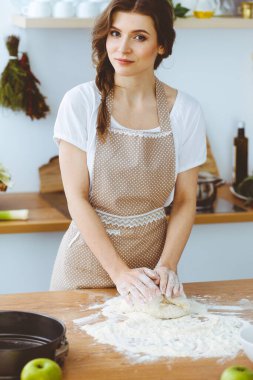 Genç esmer kadın mutfakta pizza ya da el yapımı makarna pişiriyor. Ev hanımı ahşap masada hamur hazırlıyor. Diyet, gıda ve sağlık konsepti
