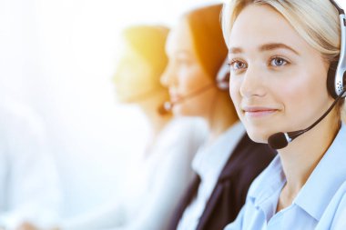 Güneşli ofiste çalışan bir grup farklı telefon operatörü. Kulaklıklı yakışıklı iş kadını müşterilere danışıyor. Çağrı merkezi ve iş adamları kavramı