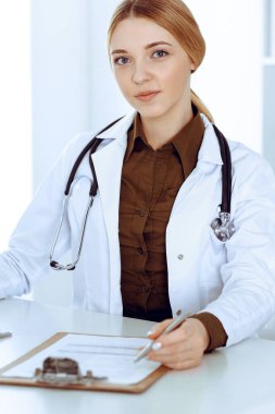 Hastanedeki genç bayan doktor masaüstü bilgisayar monitörüne bakıyor. Doktor ilaç geçmişi ve sınav sonuçlarını kontrol ediyor. Tıp ve sağlık hizmetleri kavramı