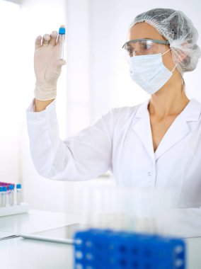 Koruyucu gözlüklü profesyonel kadın bilim adamı laboratuarda reaktörlerle araştırma tüpü kullanıyor. Tıp ve araştırma kavramları