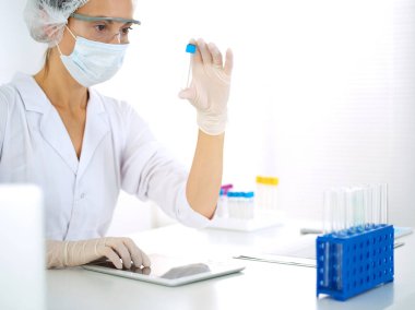 Koruyucu gözlüklü profesyonel kadın bilim adamı laboratuarda reaktörlerle araştırma tüpü kullanıyor. Tıp ve araştırma kavramları