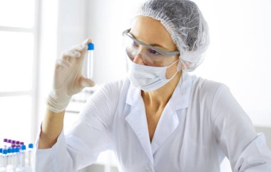 Koruyucu gözlüklü profesyonel kadın bilim adamı laboratuarda reaktörlerle araştırma tüpü kullanıyor. Tıp ve araştırma kavramları