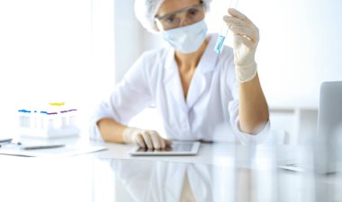 Koruyucu gözlüklü profesyonel kadın bilim adamı laboratuarda reaktörlerle araştırma tüpü kullanıyor. Tıp ve araştırma kavramları