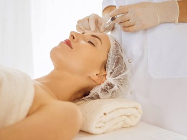 Güzel bir kadın kapalı gözlerle güzellik iğneleri yaptırıyor. Güzellik uzmanı elleri şırıngayla kadın yüzüne güzellik prosedürü uyguluyor. Kozmetik tıp ve cerrahi konsepti