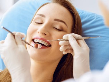 Diş hekiminde dişçi tarafından incelenen diş telleriyle gülümseyen genç bir kadın. Sağlıklı diş ve ilaç konsepti
