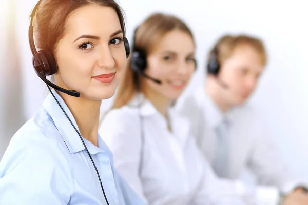 Bel het centrum. Focus op mooie zakelijke vrouw met behulp van headset in zonnig kantoor — Stockfoto