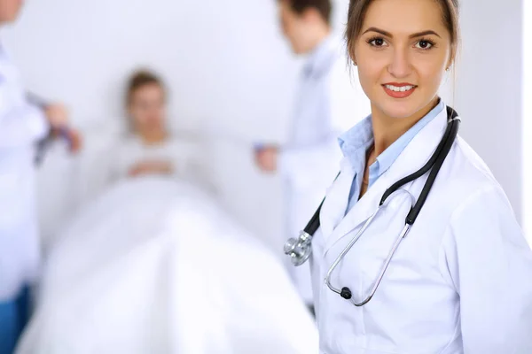 Female doctor smiling on the background with patient in the bed and two doctors