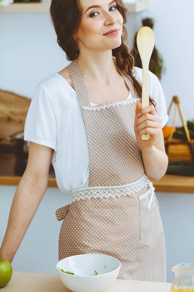 Jonge brunette die kookt in de keuken. Huisvrouw met een houten lepel in haar hand. Voedsel- en gezondheidsconcept — Stockfoto