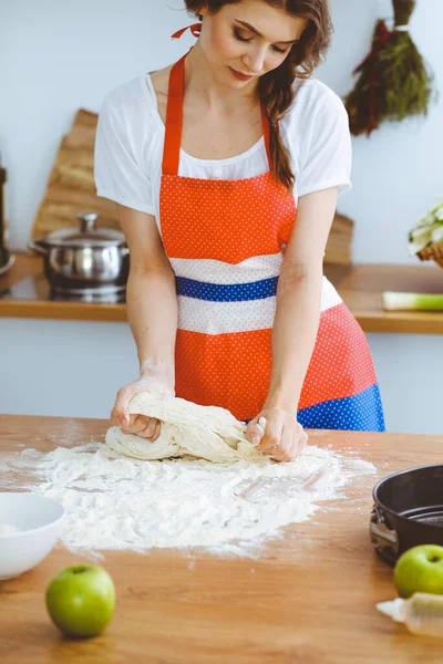 Jovem morena cozinhando pizza ou massa artesanal na cozinha. Dona de casa que prepara a massa de farinha na mesa de madeira. Conceito de alimentação, alimentação e saúde — Fotografia de Stock