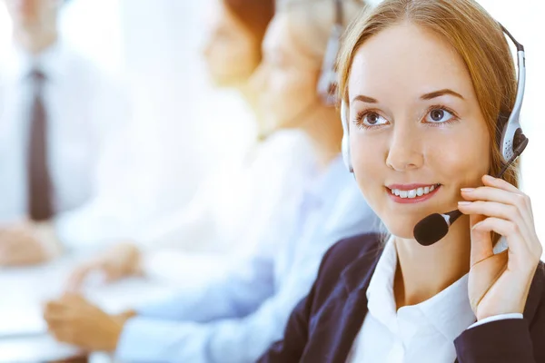 Güneşli ofiste çalışan bir grup farklı telefon operatörü. Kulaklıklı yakışıklı iş kadını müşterilere danışıyor. Çağrı merkezi ve iş adamları kavramı — Stok fotoğraf