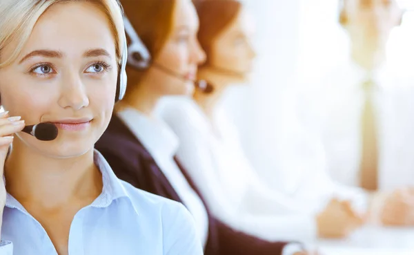 Group of diverse phone operators at work in sunny office. Handsome business woman with headphones consulting clients. Call center and business people concept