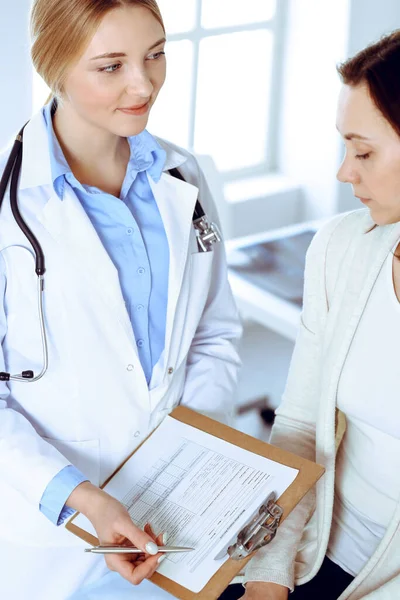 Ung kvinnlig läkare och patient vid läkarundersökning på sjukhusets kontor. Blå blus av terapeut ser bra ut. Medicin och hälsovård — Stockfoto