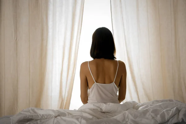 Woman stretching hands in bed after wake up, sun flare . Brunette entering a day happy and relaxed after good night sleep and back view. Concept of a new day and joyful weekend