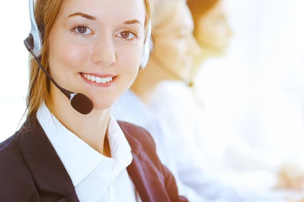 Group of diverse phone operators at work in sunny office. Handsome business woman with headphones consulting clients. Call center and business people concept Stock Picture