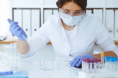 Koruyucu gözlüklü profesyonel kadın bilim adamının laboratuarda reaktörlerle deney yapması. Tıp ve araştırma konsepti
