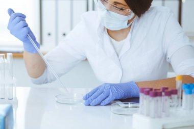 Koruyucu gözlüklü profesyonel kadın bilim adamının laboratuarda reaktörlerle deney yapması. Tıp ve araştırma konsepti