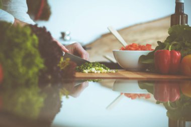 Mutfakta pişen bilinmeyen insan elleri. Yeşil soğan dilimleyen bir kadın. Sağlıklı yemek ve vejetaryen gıda konsepti.