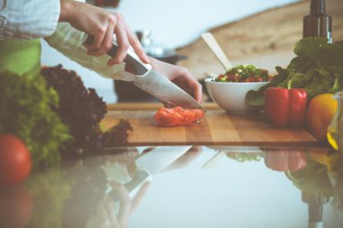 Mutfakta pişen bilinmeyen insan elleri. Kırmızı domatesleri dilimleyen kadın. Sağlıklı yemek ve vejetaryen gıda konsepti.