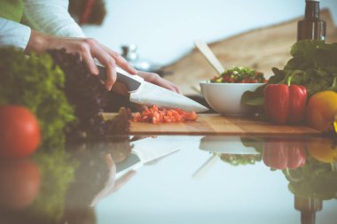 Mutfakta pişen bilinmeyen insan elleri. Kırmızı domatesleri dilimleyen kadın. Sağlıklı yemek ve vejetaryen gıda konsepti.