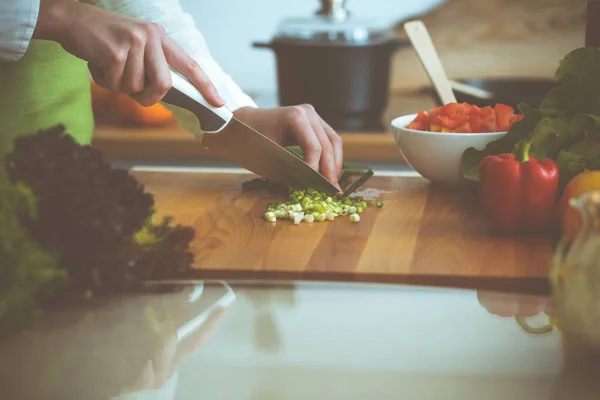 모르는 인간 손으로 부엌에서 요리하고 있어. 녹색 양파를 썰고 있는 여성. 건강에 좋은 식사와 채식 식품의 개념 — 스톡 사진