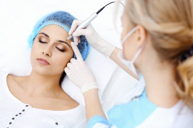 Kadın yüzüne kaş dövmesi yapan profesyonel bir güzellik uzmanı. Güzellik salonunda kalıcı kaş makyajı, yakın çekim. Kozmetoloji tedavisi