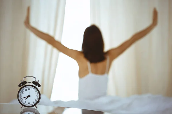 Woman stretching hands in bed after wake up, sun flare . Brunette entering a day happy and relaxed after good night sleep and back view. Concept of a new day and joyful weekend