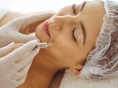 Güzellik uzmanı, genç esmer kadının yüzüne şırıngayla güzellik prosedürü uyguluyor. Kozmetik ilaç ve ameliyat, güzellik iğneleri.