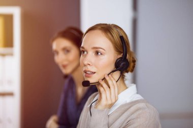 İş kadını güneşli ofiste kulaklıkla konuşuyor. Çağrı merkezi ve çeşitli iş grupları