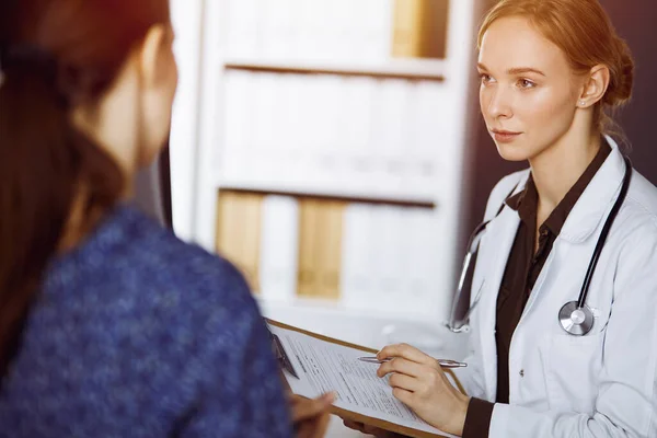 Joyeux sourire femme médecin et patiente discutant de l'examen de santé en cours tout en étant assis dans une clinique ensoleillée. Concept de médecine — Photo