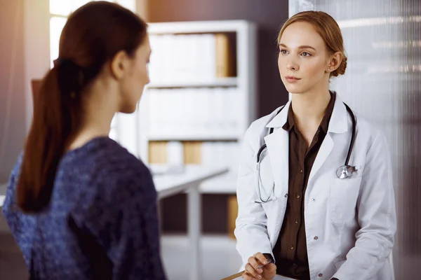 Joyeux sourire femme médecin et patiente discutant de l'examen de santé en cours tout en étant assis dans une clinique ensoleillée. Concept de médecine — Photo