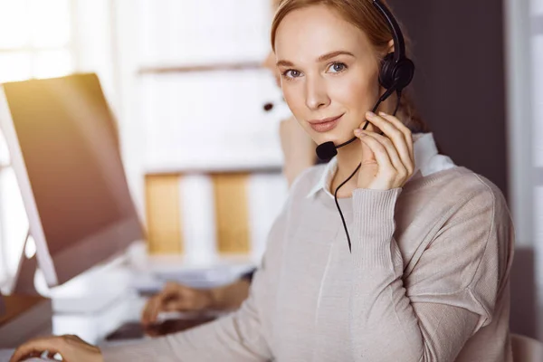 Mujer de negocios hablando con auriculares en la oficina soleada. Centro de llamadas y grupo de personas diversas en los negocios — Foto de Stock