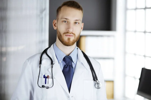 赤ひげの医者は彼の職場の近くの診療所にまっすぐ立っている。医師の肖像画。医学と医療の概念 — ストック写真