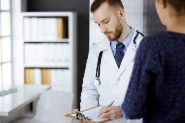 Dost canlısı kızıl sakallı doktor ve hasta kadın klinikte otururken sağlık muayenesini tartışıyorlar. Mükemmel tıbbi hizmet ve tıp konsepti