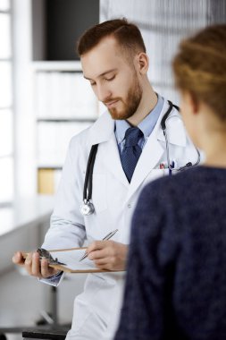 Dost canlısı kızıl sakallı doktor ve hasta kadın klinikte otururken sağlık muayenesini tartışıyorlar. Mükemmel tıbbi hizmet ve tıp konsepti