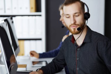 Modern ofiste otururken kulaklıkla konuşan kızıl sakallı bir iş adamı. Çağrı merkezinde çeşitli insanlar var. Tele pazarlama ve müşteri hizmetleri