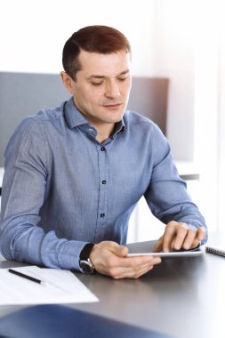 Modern ofiste tablet bilgisayarla çalışan bir iş adamı. İş yerindeki erkek girişimcinin ya da şirket müdürünün vesikalığı. İş konsepti