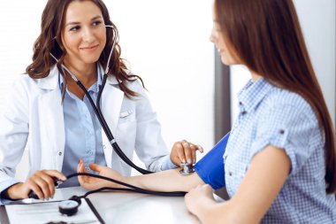Elinde steteskop olan bir doktor kadın hastasını muayene ediyor. Sağlık, kardiyoloji ve tıp kavramları