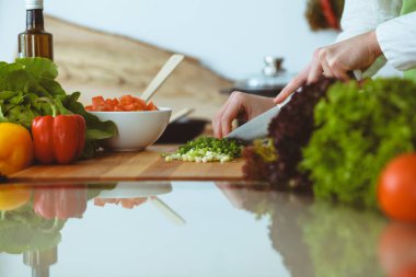 Mutfakta pişen bilinmeyen insan elleri. Yeşil soğan dilimleyen bir kadın. Sağlıklı yemek ve vejetaryen gıda konsepti.