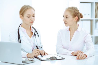 Doktor ve hasta masada otururken hastane ofisinde konuşuyorlar. Tıp alanında sağlık ve müşteri hizmetleri