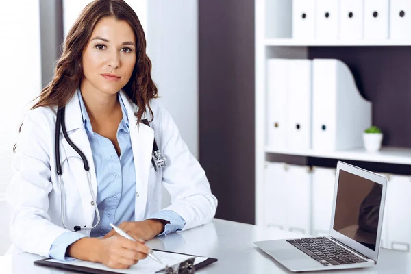 Mujer doctora llenando formulario médico mientras está sentada en el escritorio en la oficina del hospital. Médico trabajando. Concepto de medicina y salud — Foto de Stock