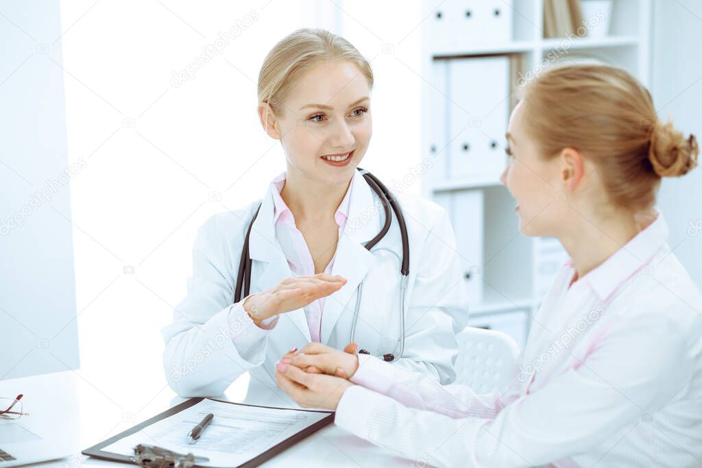 Doctor and patient talking in hospital office while sitting at the desk. Health care and client service in medicine