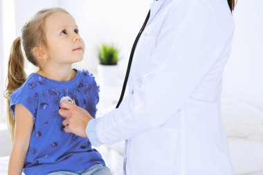 Doktor steteskopla küçük bir kızı muayene ediyor. Her zamanki tıbbi muayenede gülümseyen çocuk hasta. Tıp ve sağlık hizmetleri kavramları