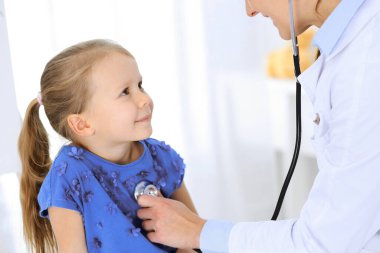 Doktor steteskopla küçük bir kızı muayene ediyor. Her zamanki tıbbi muayenede gülümseyen çocuk hasta. Tıp ve sağlık hizmetleri kavramları